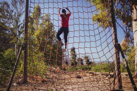 Female Athlete Climbing Red Cargo Net in Outdoor Adventure