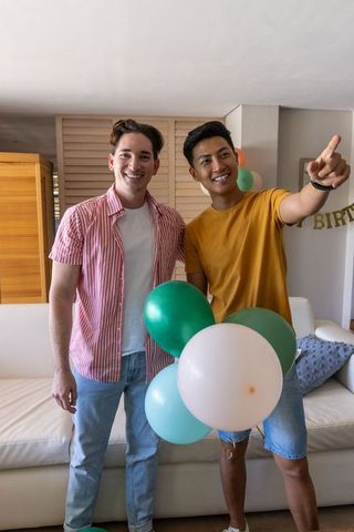Two friends celebrating birthday at home smiling and holding green white balloons