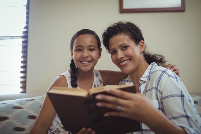 Mother and daughter reading book in living room at home