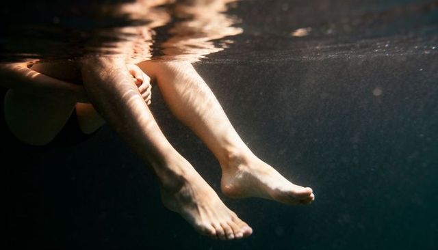 Floating legs and feet beneath water surface with sunlight caustics and ripples