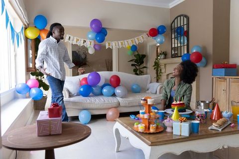 Couple celebrating birthday with colorful balloons cake and gifts in sunlit living room