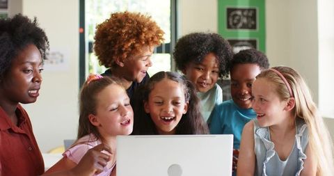 Teacher Guiding Diverse Children Gathering Around Laptop Smiling and Collaborating