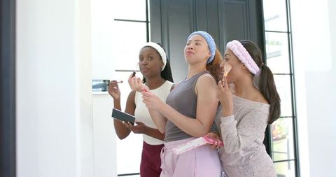 African american friends applying makeup at home wearing headbands and using palettes