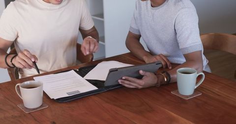 Young colleagues reviewing contract with tablet and coffee at wooden table in casual office