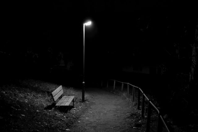 Desolate pathway lit by a single lamp post with an unoccupied bench at night. Captures a mood of loneliness and solitude, suitable for themes of introspection, mystery, and urban solitude. Ideal for illustrating stories, blog posts, or mental health concepts.