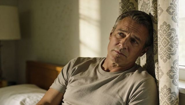 Contemplative middle-aged man leaning on patterned curtains by window, soft daylight mood
