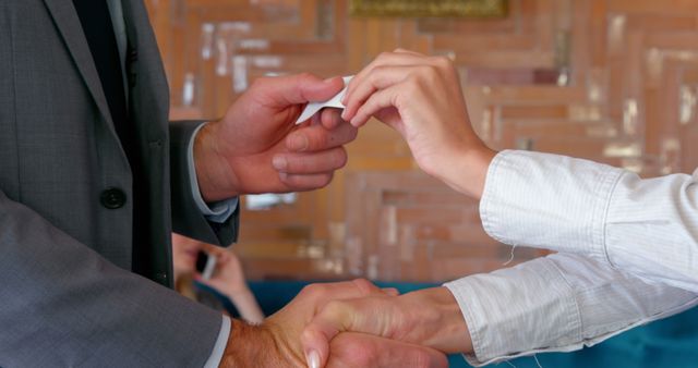 Close-up of two people exchanging business cards during a professional handshake at a business meeting. Suitable for illustrating topics related to networking, professional connections, business etiquette, corporate meetings, employment opportunities, and relationship building in a professional context.