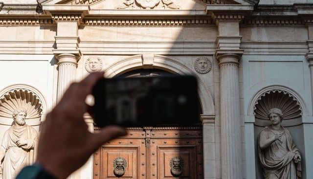 Framing smartphone capturing ornate doorway with lion-head knockers and classical statues