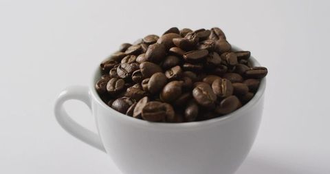 Minimalist white mug overflowing dark roasted coffee beans for gourmet branding