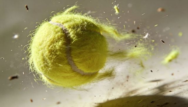 High-speed close-up of spinning fuzzy tennis ball with flying debris and dynamic motion