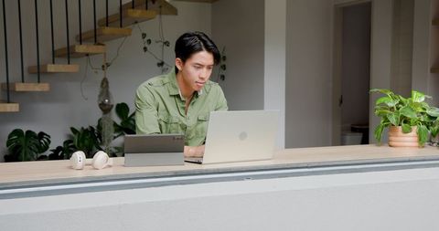 Man typing on laptop at home counter with greenery and modern decor