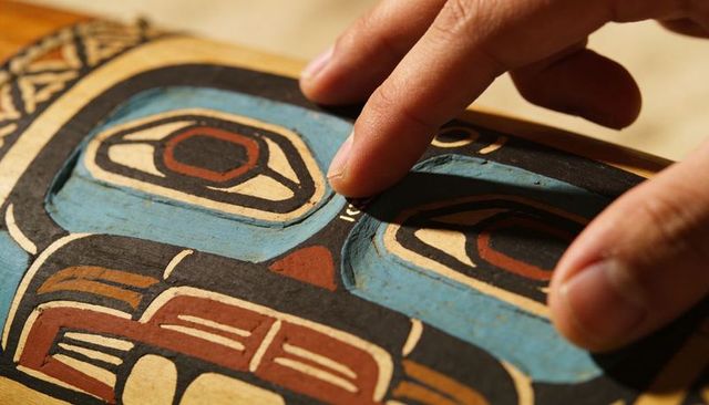 Fingertips tracing handcrafted painted carved wooden mask showing worn texture and grain