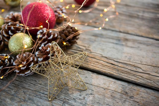Close-up of festive Christmas decorations including a golden wire star, pine cones, illuminated fairy lights, and colorful baubles on a rustic wooden surface. Perfect for holiday greeting cards, festive advertisements, or decoration inspiration.