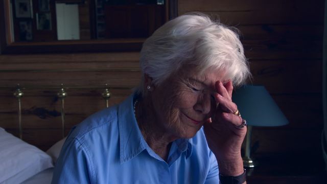 An elderly woman with a crestfallen expression is sitting on a bed, reflecting feelings of sadness or frustration. Her disheartened gesture suggests introspection or worry, captured in a domestic-bedroom environment. This can be used in themes highlighting emotional moments among seniors, geriatric studies, or mental health awareness in older adults.