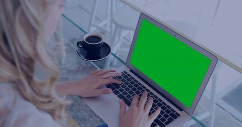 Blonde woman typing on laptop with green screen at modern cafe workspace for remote work