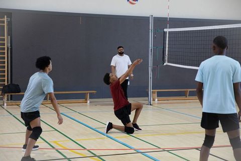 Teen male volleyball team training indoor gym coach guiding kneeling player reaching ball