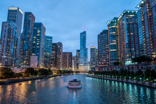 A cityscape featuring an architectural boat tour on the Chicago River at dusk. This scene captures the blend of modern and historic skyscrapers illuminated against the evening sky. Ideal for promoting tourism, city tours, or travel experiences. Suitable for use in travel brochures, websites, or urban studies presentations.