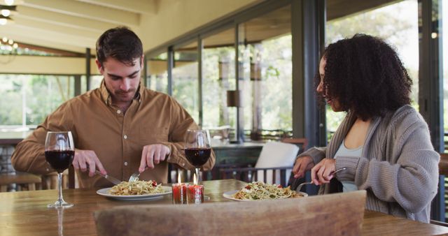 Couple enjoying a romantic dinner with pasta and red wine at a modern restaurant. Ideal for use in websites and advertisements focusing on relationships, romantic dining experiences, gourmet food, and lifestyle content.