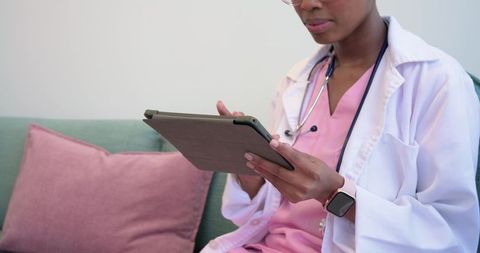 African clinician tapping tablet for telemedicine consultation in pink scrubs and lab coat
