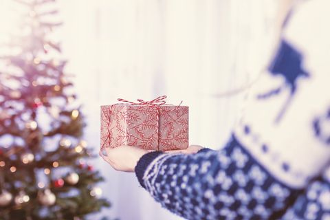 Open Hands Offering Holiday Gift Beside Decorated Christmas Tree