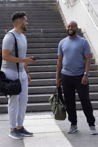 African american men meeting and smiling after workout on urban steps carrying gym bags