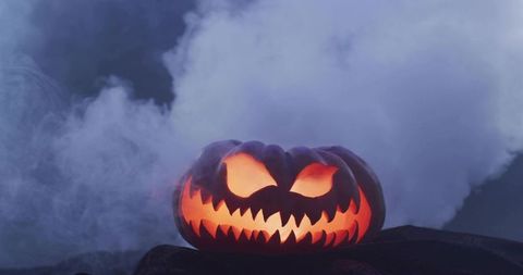 Glowing carved jack-o'-lantern casting sinister grin through misty fog emitting warm orange light