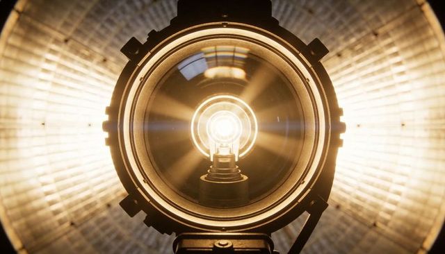 Studio spotlight casting warm radial light through lens with visible halogen filament