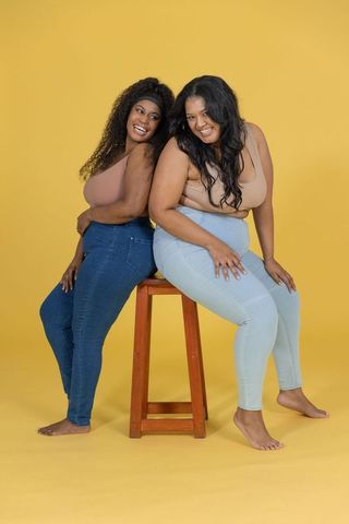 Plus-size diverse women smiling and posing back-to-back in denim and tanks on yellow