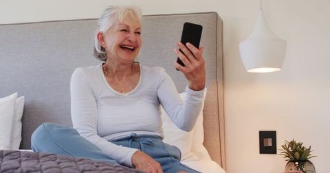 Smiling senior woman relaxing with smartphone on bed