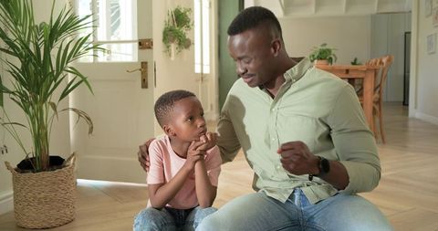African american father comforting and encouraging son while sitting on floor near doorway