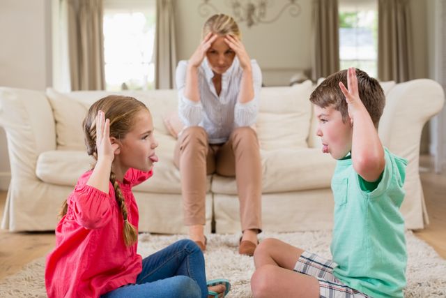 Frustrated mother sitting on sofa while her children tease each other on the floor. The scene captures the challenges of parenting and family dynamics. Useful for articles on parenting, family relationships, childhood behavior, and stress management.