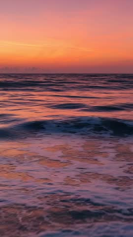 Vertical video showing ocean waves cresting and breaking at sunset with pink sky