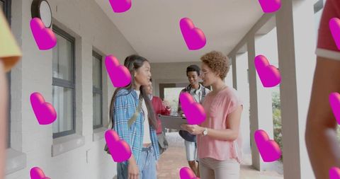 Student talking with tutor holding tablet in school hallway with floating pink hearts