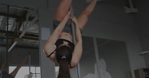 Woman Performing Inverted Pole Dance Move at Fitness Studio