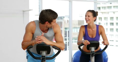 Fit couple exercising on stationary bikes in fitness studio