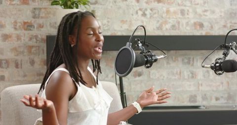 African american woman recording energetic podcast, gesturing in minimalist brick studio
