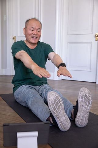 Senior asian man doing seated stretching workout at home with tablet