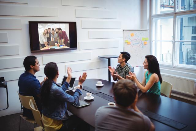 Business professionals sitting around a conference table, applauding during a video conference. Ideal for illustrating remote work, corporate meetings, teamwork, and digital communication in a professional setting.