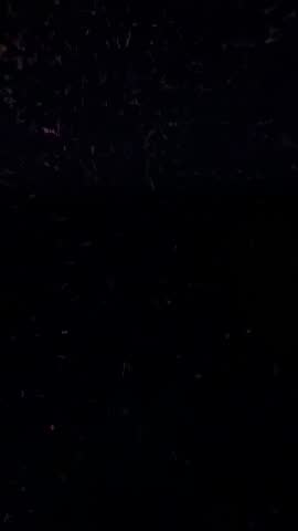 Emerging pink glow revealing drifting luminescent particles in dark void vertical video