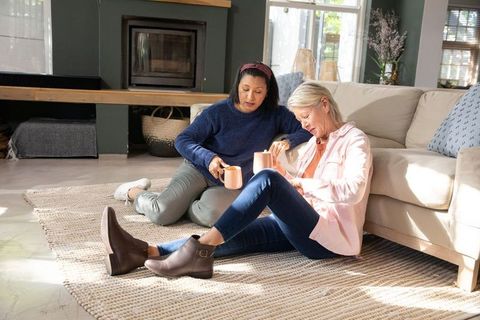 Mature friends relaxing on living room rug, sharing coffee while choosing decor swatches