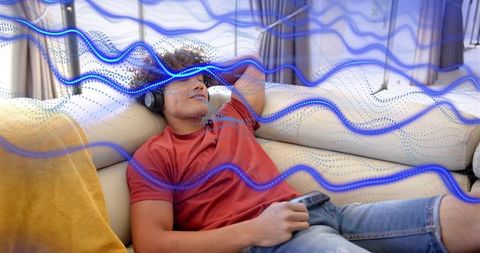 Listening to music on sofa with headphones and blue sound wave overlay