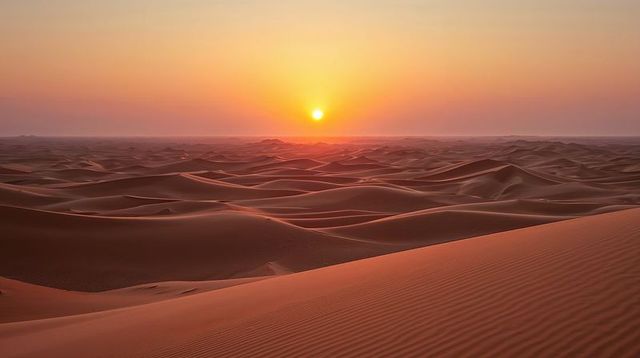 Sun lowering over expansive sand dunes casting warm golden glow across desert expanse