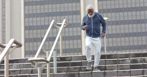Senior african american man descending city stairs wearing navy hoodie and gray joggers