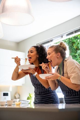 Diverse friends tasting homemade noodles in modern kitchen