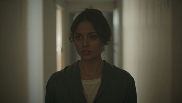 Standing woman looking pensive in narrow corridor with warm backlight and moody portrait