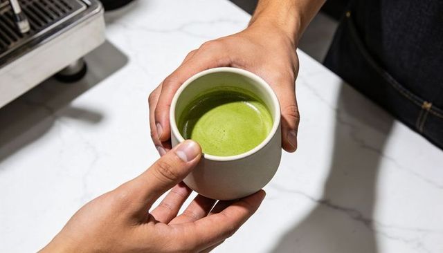 Barista passing matcha cup to customer over marble counter