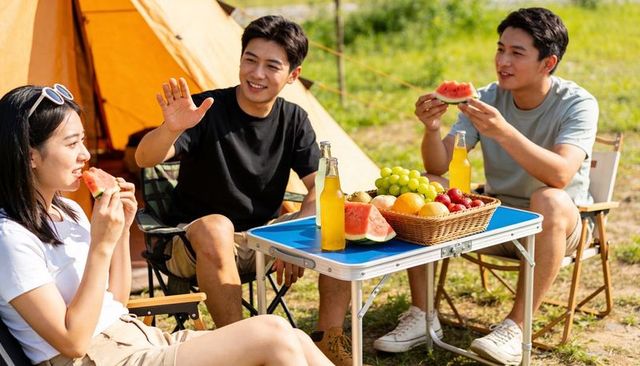 Friends enjoying watermelon and fresh fruit while camping by bright yellow tent
