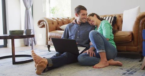 Cheerful couple paying bills online relaxing at home