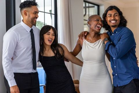 Diverse friends laughing and linking arms in elegant home celebration wearing formal attire