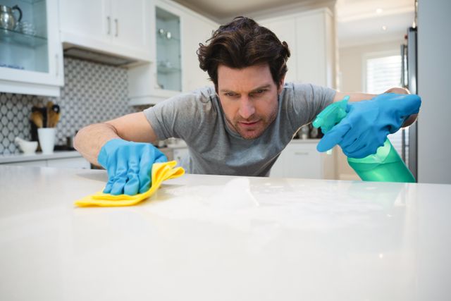 Young man cleaning kitchen worktop at home